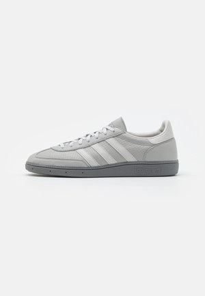 Lysegrå Adidas sneaker med hvide striber, snøredesign, tekstureret sål og Adidas-logo på siden.