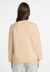 Beige kötött pulóver laza szabással, virágmintás hímzéssel az ujjain és bordás szegéllyel. Nem látható márkajelzés.