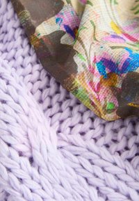 Tissu tricoté violet superposé à un tissu à motif floral dans des tons beige, rose et vert, présentant une texture lisse et un tissage complexe.