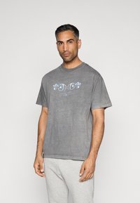 T-shirt cinza de algodão com um corte descontraído, apresentando um design gráfico colorido na frente. Mangas curtas, decote redondo, textura suave.