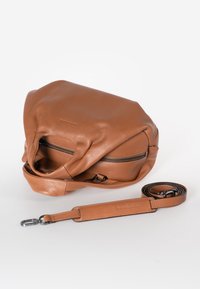 Bruine leren handtas met een textuurafwerking, een ritscompartiment en een verstelbare schouderriem ernaast gelegd. Zachte, afgeronde vorm.
