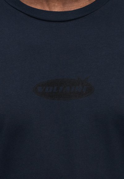 Námořnicky modré bavlněné tričko s kulatým výstřihem, ve středu zdobené jemným černým potiskem loga. Měkká textura, volný střih.