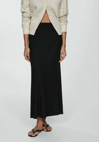 Sort ankel-længde nederdel med en svungen bund. Kombineret med en lys beige linned button-up jakke. Fodtøjet består af sorte flade sandaler.