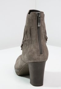 Bottines en daim grises avec un talon empilé. Dotées d'une fermeture éclair sur le côté et de franges à l'arrière. La semelle texturée améliore l'adhérence.