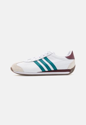 White low-top sneaker with teal stripes, beige suede toe cap, and maroon heel against plain light background.