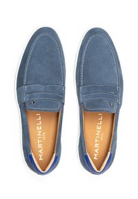 Mocasines de ante azul con suelas blancas y acentos en azul contrastante. Presentan detalles cosidos y un forro interior suave. Logo de la marca visible.