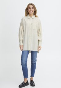 Long-sleeve, collared shirt in cream and light yellow stripes, featuring a patch pocket. Worn with blue jeans and black loafers.