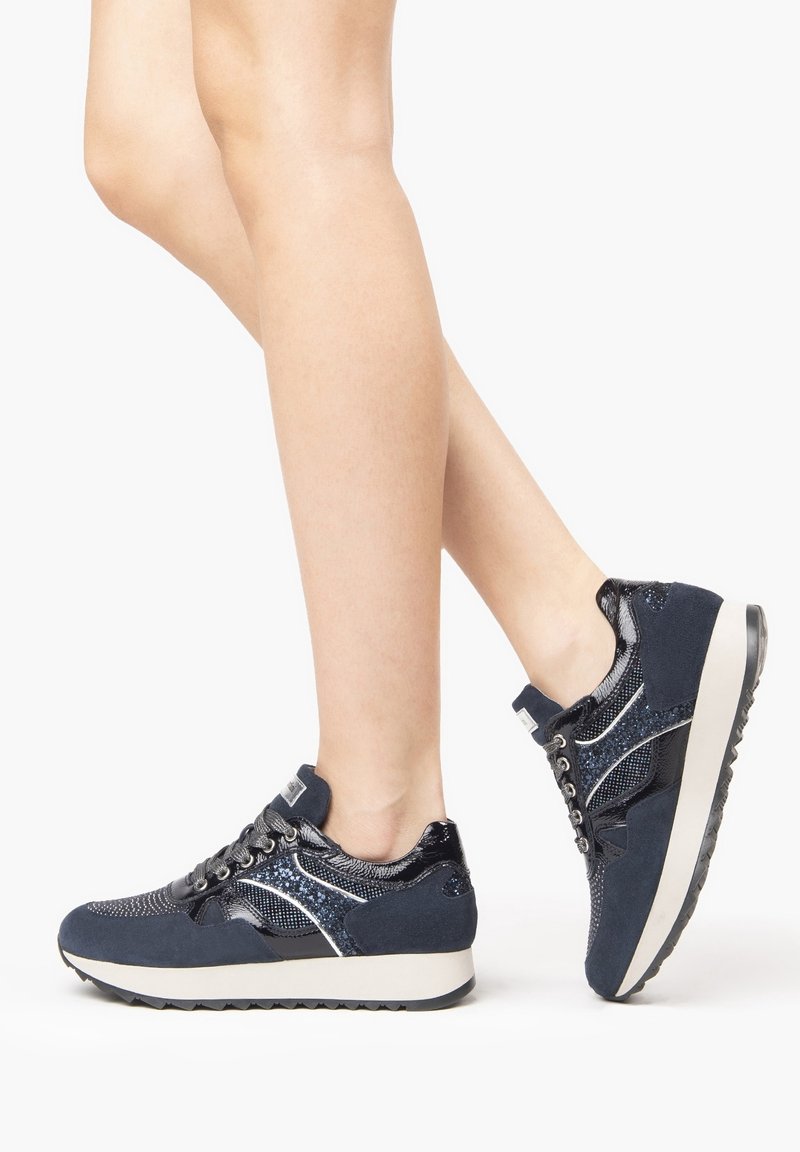 Námořnické modré tenisky s kombinací hladkých a texturovaných materiálů, kovovými akcenty, šněrovacím designem a silnou bílou podrážkou.