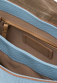 Interno della borsa in pelle con un rivestimento blu texturizzato, tessuto marrone liscio e un'etichetta stampata con "Gianni Chiarini, Made in Italy."