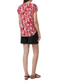 Blouse rouge et blanche à motif, à manches courtes, avec un ourlet arrondi et une coupe ample, associée à un short noir et des sandales plates.