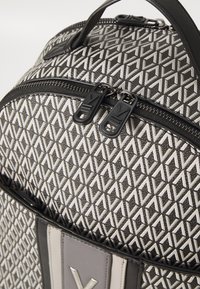 Ruksak s geometrijskim uzorkom od crno-bijelog platna. Sadrži dvostruki patentni zatvarač, kožne detalje i teksturiranu površinu.