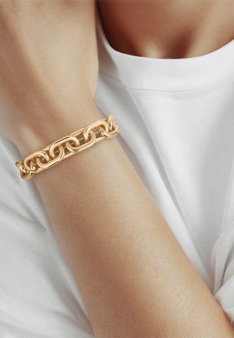 Guld kædelink armbånd båret på håndleddet af en person iført en hvid skjorte.