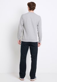 Hellgrauer Sweatshirt mit langen Ärmeln und Rundhalsausschnitt, kombiniert mit dunkelblauen Hosen und Sneakers. Einfaches Design mit gerippten Bündchen und Saum.