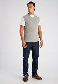 Grå stickad väst med V-ringning över en vit T-shirt, i kombination med mörkblå jeans och bruna snörskor av båttyp.