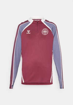 Bordó hosszú ujjú sportmez fél cipzárral, fehér díszítéssel és csíkos kék ujjal. Kerek logóval rendelkezik a mellkasán.