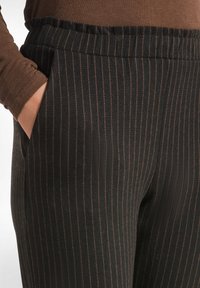 Pantalones a rayas negras hechos de una tela elástica con una cinturilla y bolsillos laterales. Presenta delgadas rayas verticales marrones para contraste.