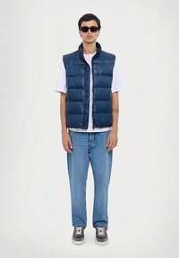 Tumesinine puffer-liiv, millel on horisontaalne õmblus, kantud valge T-särgi peale. Sobitatud helesiniste teksade ja tumedate tossudega. Aksessuaarideks päikeseprillid.