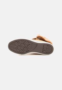 Calzature color marrone chiaro con suola in gomma strutturata, sottopiede bianco e bordo superiore morbido. Presenta una battuta con motivo per una buona aderenza.