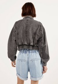 Grå kort denimjacka med rynkad nederkant, oversized ärmar och kontrasterande sömmar, ihopparad med ljusblå rullade denimshorts.