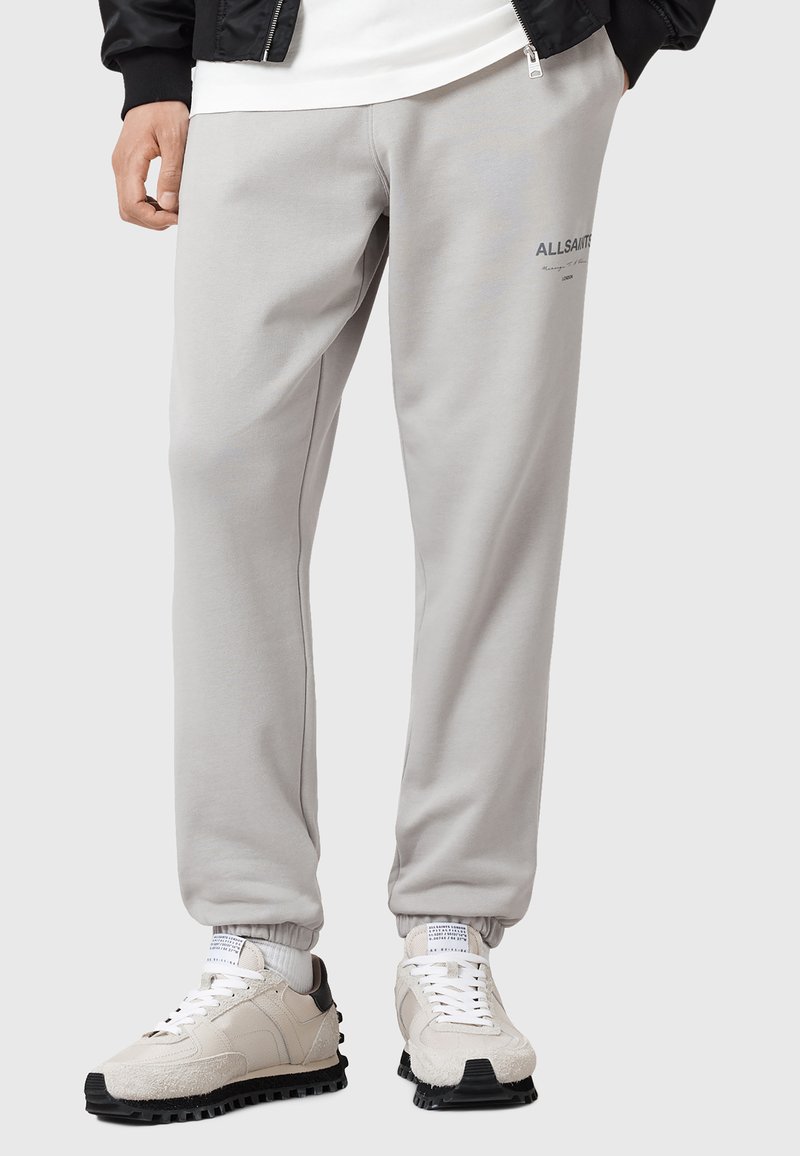 Grijze sweatpants met een elastische tailleband, zijzakken en een subtiele logo op de linkerdij, gecombineerd met lichte sneakers.