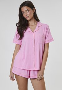 Rosa pyjamas-set med kort ärm, som består av en knapp-up topp med ficka och orange piping, tillsammans med matchande shorts. Mjuk tygtextur.