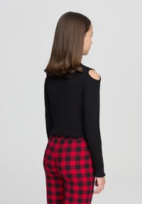 Top nero a maniche lunghe con dettaglio spalle scoperte abbinato a leggings a quadri rossi e neri, che mostrano un design aderente.