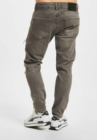 Faded gray denim jeans with a slim fit, featuring two back pockets, distressed details on the legs, and a black waistband tag.