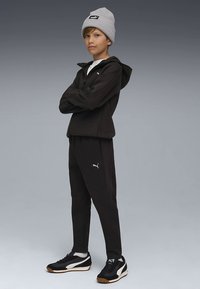 Črn športni komplet s kapuco, siva pletena kapa in črni supergi z belimi poudarki in logotipi. Mehka tekstura tkanine.