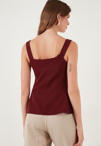 Bordo bezrukavni top s kvadratnim izrezom, izrađen od glatkog materijala. Ima široke naramenice i uski kroj s blagim izrezom.