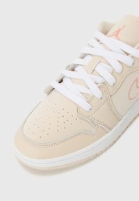 Beige nahast tennisetossud valgete paeltega, perforeeritud varbaosaga ja heledate hallide aktsentidega. Küljel on persika värvi logo ja valge tald.