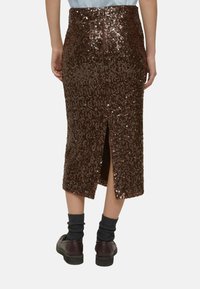 Brauner Midirock mit Pailletten, hinten mit Schlitz und Reißverschluss. Kombiniert mit dunklen Socken und braunen Schuhen, die die strukturierte Oberfläche betonen.