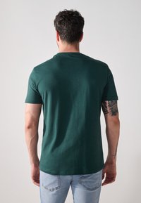 Groene T-shirt met korte mouwen, gemaakt van katoen, met een ronde hals en een gladde textuur, bekeken vanaf de achterkant met een eenvoudig ontwerp.