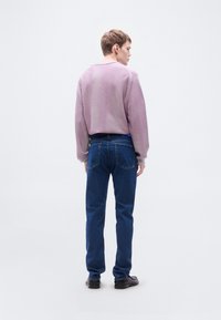 Ανοιχτό μωβ πλεκτό πουλόβερ με στρογγυλή λαιμόκοψη και υφασμένα μανίκια, συνδυασμένο με σκουρό μπλε τζιν και μαύρα παπούτσια, από την πίσω όψη.