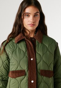 Quilted green jacket with brown corduroy collar, front placket, and pockets. Features smooth texture and rounded stitching patterns.