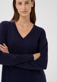 Marineblauer V-Ausschnitt-Pullover aus weichem Stoff, mit langen Ärmeln und lockerem Schnitt. Schlichtes Design mit klaren Linien und minimalen Details.