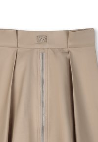 Jupe plissée beige avec une texture lisse, dotée d'un détail en fermeture éclair argentée au centre et d'une étiquette de logo discrète sur la taille.