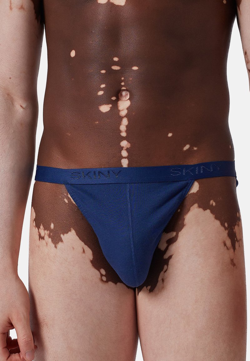 Mörkblå herrtanga tillverkad av mjuk tyg med SKINY-logotyp på midjebandet. Har en slät yta och en konturerad form.