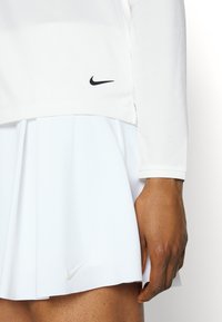 Vestito da tennis bianco con gonna plissettata, maniche lunghe e accenti neri del logo Nike. Realizzato in un tessuto leggero e morbido.