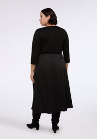 Černé šaty s třičtvrtinovými rukávy, přiléhavým korzetem a splývavou sukní. Hladká textura s elastickým pasem pro pohodlí.