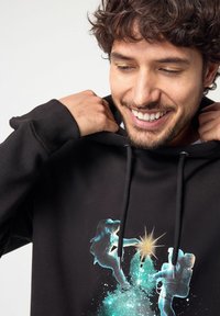 Felpa nera con cappuccio che presenta un design grafico di due figure che si allungano verso una stella, il tutto ambientato in uno sfondo cosmico con accenti blu e verdi.