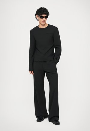 Musthave musta pika varrukaga topp ümarate kaelustega, millele on lisatud laiad mustad püksid; mõlemad on siledast kangast. Aksessuaarideks on mustad prillid.