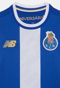 Camisa de futebol azul e branca com textura em malha, apresentando um decote redondo, logotipo "N" em dourado e brasão do FC Porto no lado esquerdo.