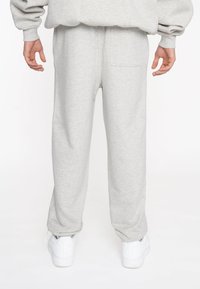 Pantalones de chándal grises hechos de tela suave, con cinturilla elástica, piernas rectas y un bolsillo trasero. Combinados con zapatillas blancas.