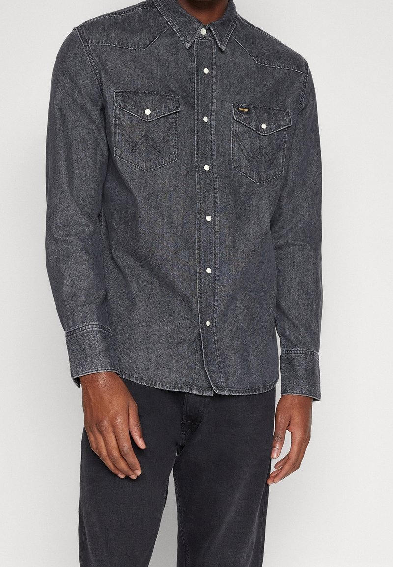 Tummansininen farkkupaita pitkillä hihoilla, joissa on kaksi rintataskua, terävä kaulus ja valkoiset nepparit. Tyylissä on hienovarainen tekstuuripinta.