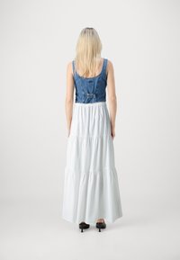 Denim top s prilagođenim korzetom i podesivim trakama na leđima, u kombinaciji s lepršavom, višeslojnim bijelim maksi suknjom i izduženim crnim štiklama.