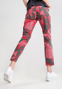 Rode broek met groene bladeren en witte grafische patronen, taps toelopende fit, voor- en achterkant zakken, gecombineerd met witte platform sneakers.