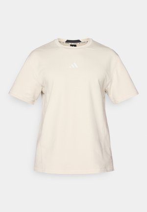 Beige cotton t-shirt with short sleeves, crew neck, and a subtle white Adidas logo on the chest. Smooth texture with minimal seams.