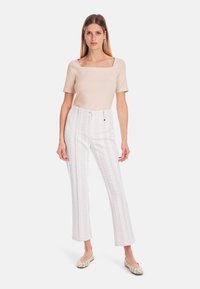 Beige square-neck top paired with white patterned trousers featuring a leaf design; model wears light, embellished flat shoes.