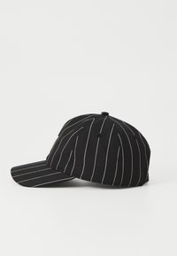 Svart caps med vertikale hvite striper, rund krone og buet skjerm. Laget av stoff, har det et enkelt design uten synlige logoer.