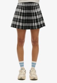 Zwart-witte geplooide geruite rok, tot halverwege het bovenbeen, gecombineerd met lichtgrijze sokken met blauwe strepen en beige sneakers.